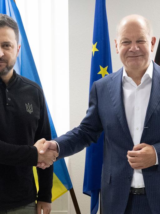 Bundeskanzler Olaf Scholz und der ukrainische Präsident Wolodymyr Selenskyj geben sich bei einem Treffen auf dem Frankfurter Flughafen die Hand und schauen in die Kameras. 