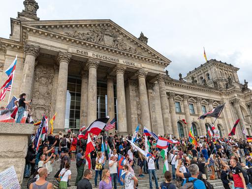 Teilnehmer einer Kundgebung gegen die Corona-Maßnahmen stehen auf den Stufen zum Reichstagsgebäude, zahlreiche Reichsflaggen sind zu sehen.