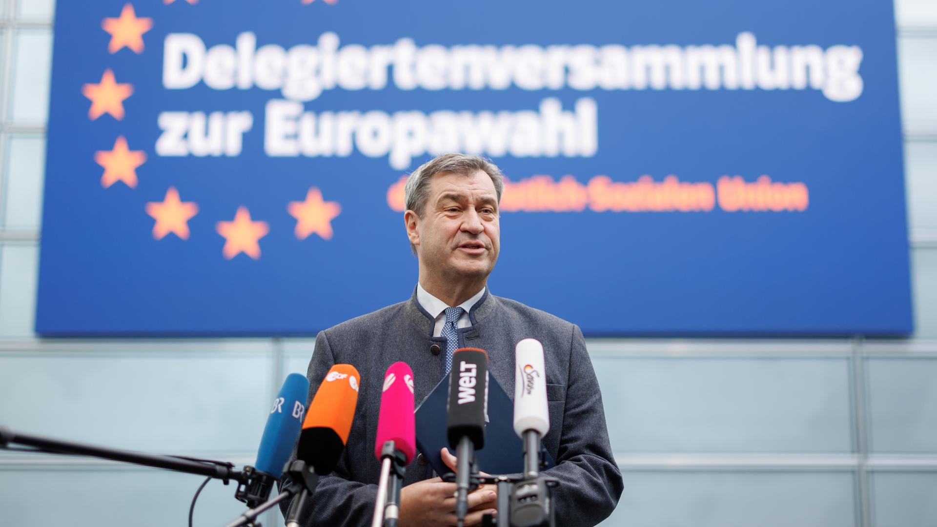 Markus Söder (CSU), Ministerpräsident von Bayern, spricht zu Journalisten. Vor ihm sind mehrere Mikrofone aufgestellt. Hinter ihm ist ein Banner mit der Aufschrift "Delegiertenversammlung zur Europawahl".