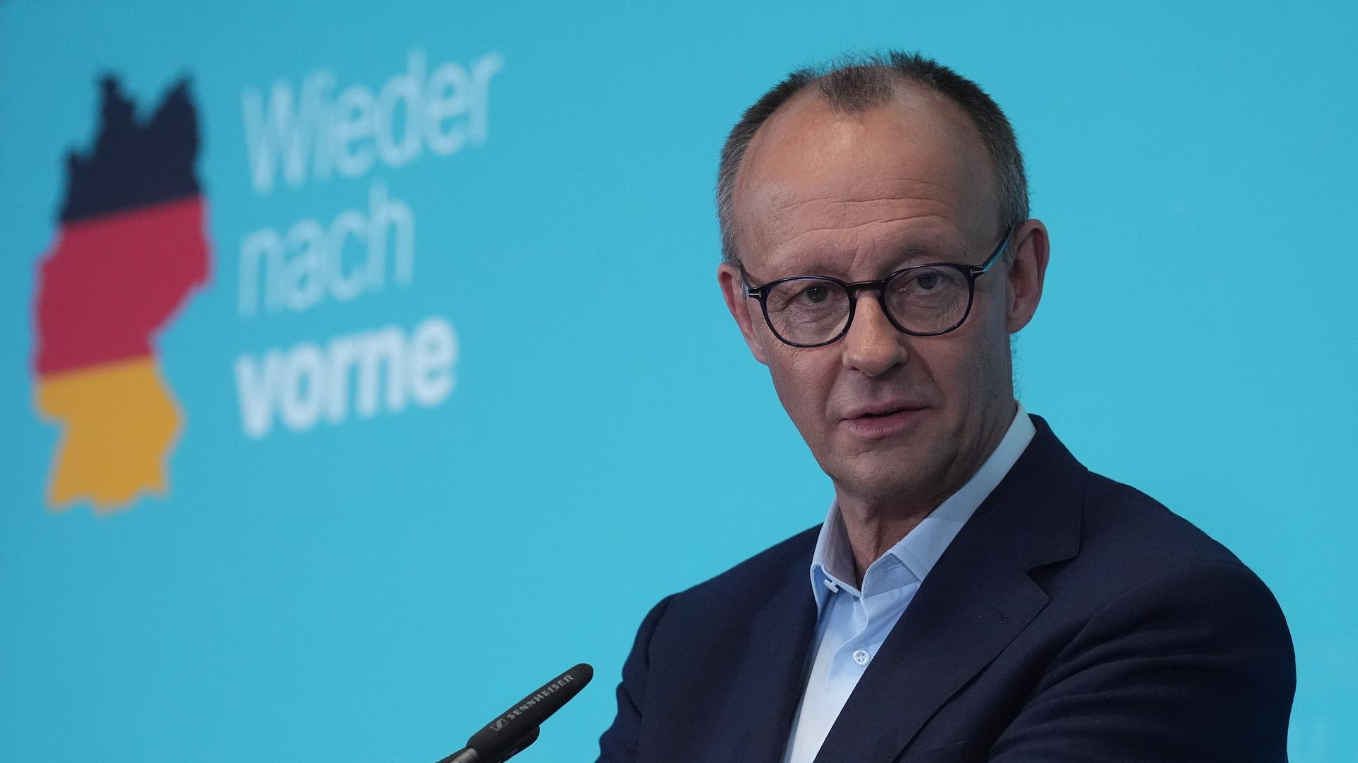 Friedrich Merz steht an einem Redepult und beantwortet Fragen von Journalisten. Im Hintergrund ist ein Wahlspruch der CDU auf einer Wand zu sehen, der "Wieder nach vorne" lautet.