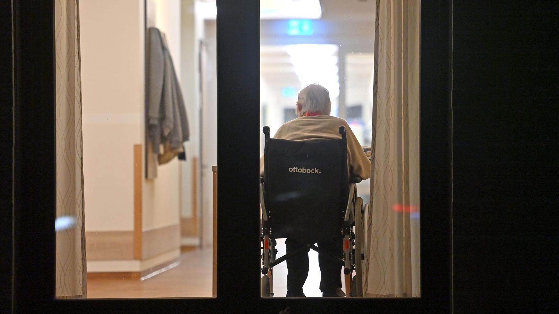 Blick auf eine Person im Rollstuhl in einem Flur in einem Altenheim im Landkreis München. 