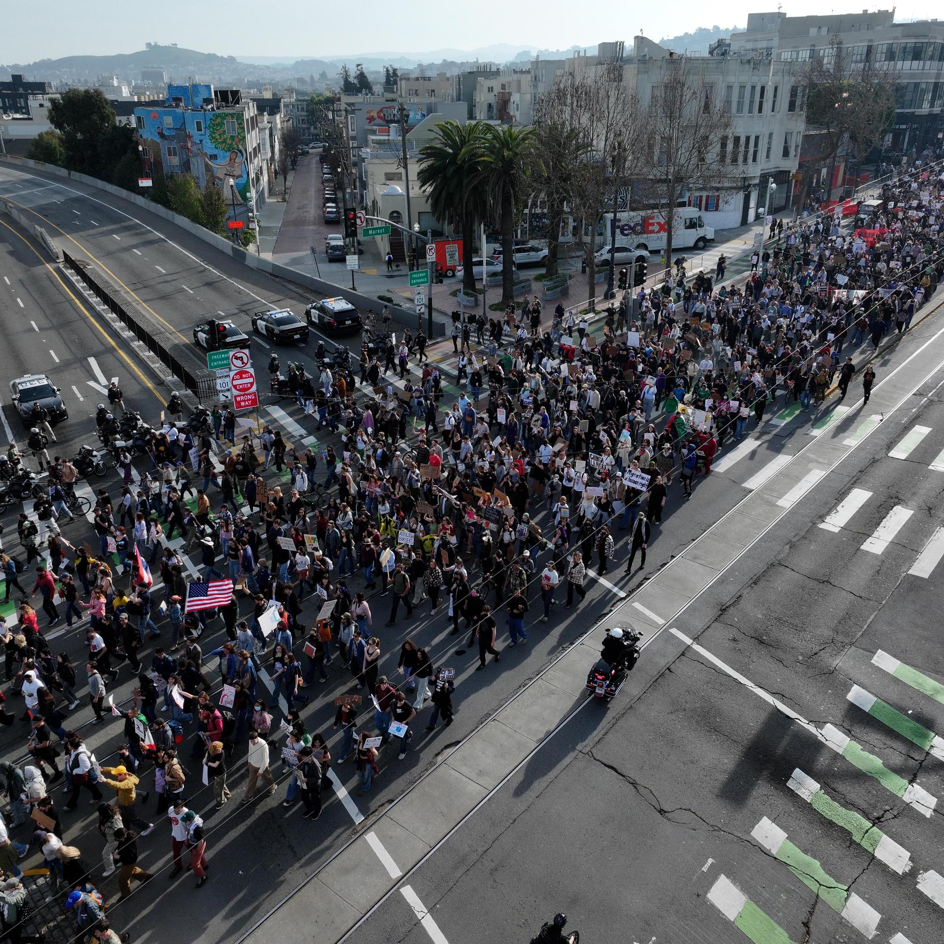 Ein Demonstrationszug mit Fahnen und Bannern zieht durch eine große Hauptverkehrsstraße in San Francisco