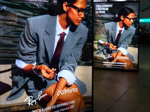 Ein Werbedisplay mit Werbung für die neue Meta-Brille von Ray Ban. Eine Frau mit Anzug und Krawatte trägt die Brille.