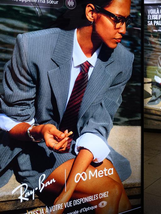 Ein Werbedisplay mit Werbung für die neue Meta-Brille von Ray Ban. Eine Frau mit Anzug und Krawatte trägt die Brille.