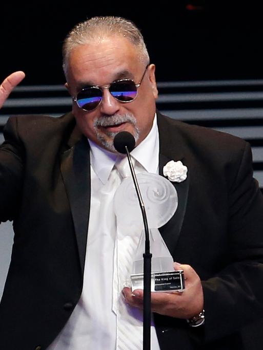 Der Musiker Willie Colon bei der Entgegennahme eines Preises in Mexico City. Er trägt eine Sonnenbrille. Die Auszeichnung hält er in der linken Hand, die rechte hat er wie zum Gruß erhoben. 