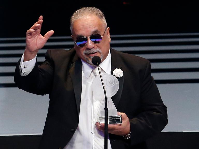 Der Musiker Willie Colon bei der Entgegennahme eines Preises in Mexico City. Er trägt eine Sonnenbrille. Die Auszeichnung hält er in der linken Hand, die rechte hat er wie zum Gruß erhoben. 