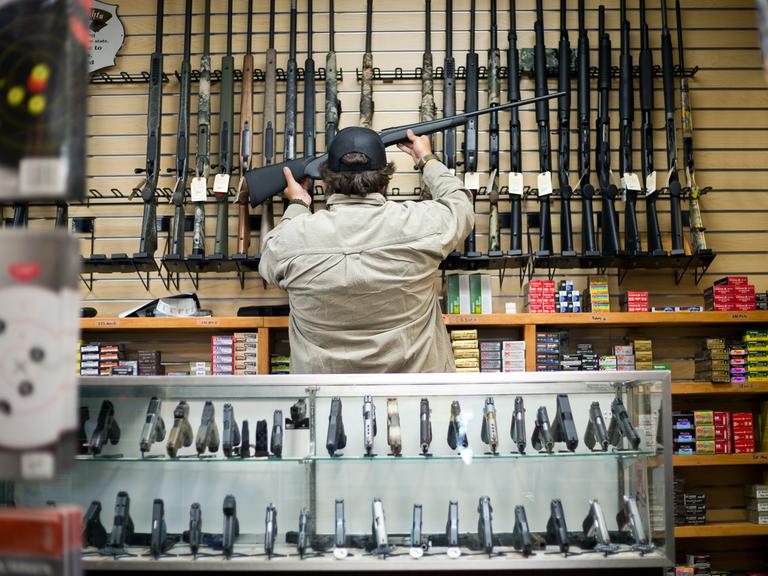 Ein Waffenhändler nimmt ein Gewehr von einem Regal in einem Waffenladen.