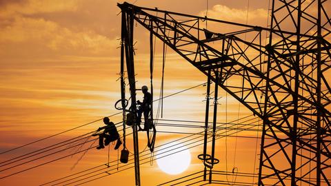 Monteure arbeiten an einem Hochspannungsmast bei Sonnenuntergang in Baden-Württemberg