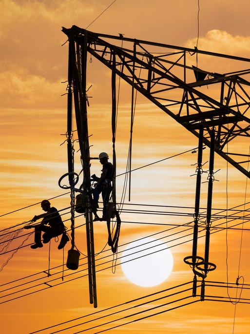 Monteure arbeiten an einem Hochspannungsmast bei Sonnenuntergang in Baden-Württemberg Monteure arbeiten an einem Hochspannungsmast bei Sonnenuntergang in Baden-Württemberg