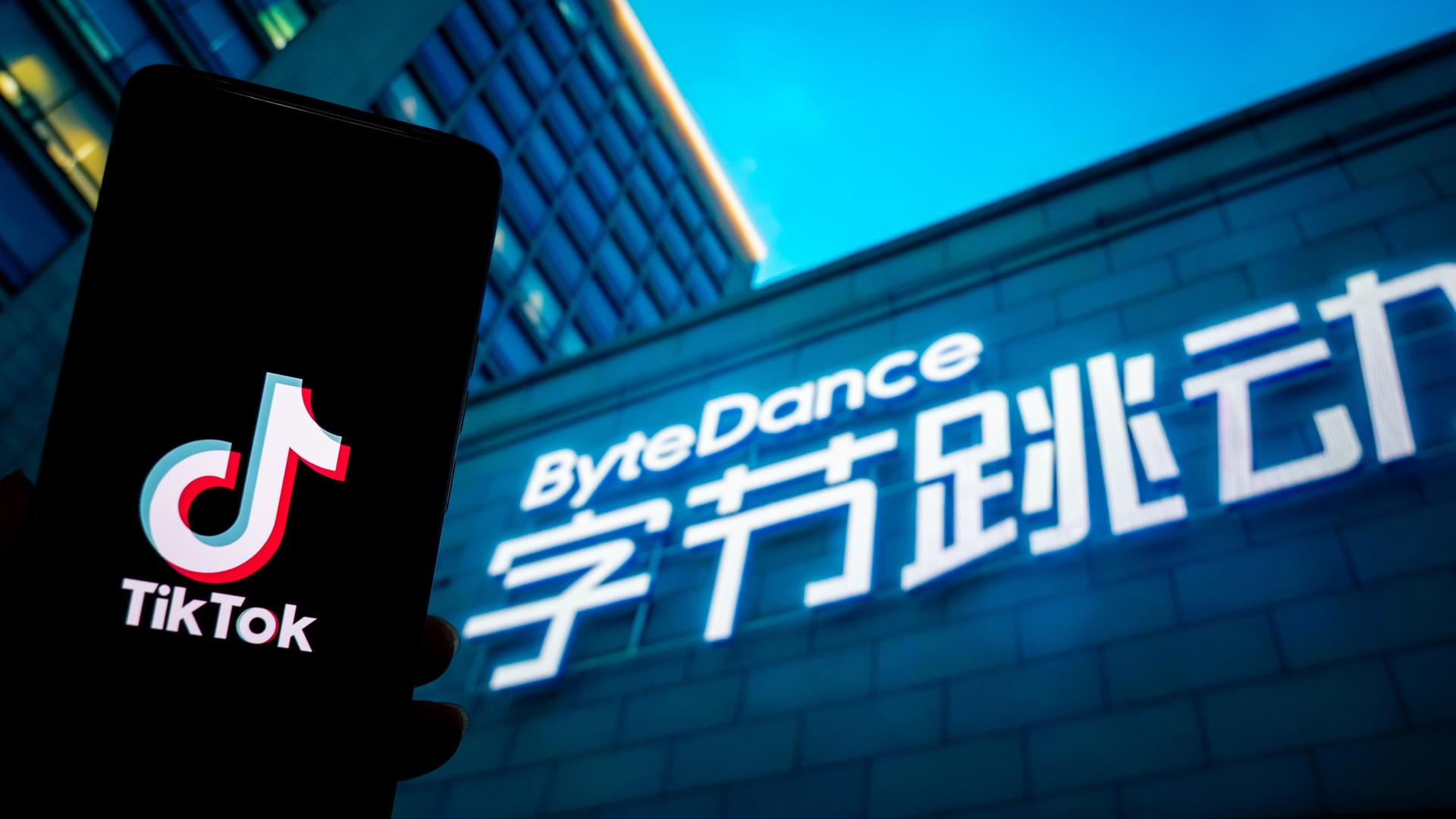 Ein Tiktok-Logo wird auf einem Smartphone neben dem Firmenlogo des chinesischen Konzerns, ByteDance, dem die Kurzvideo-Plattform gehört, angezeigt. Das Firmenlogo befindet sich an einem Gebäude, vermutlich dem Firmensitz des Technologieunternehmens.