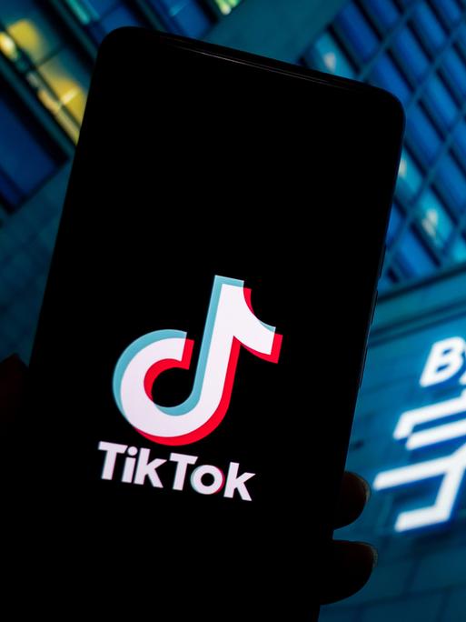 Ein Tiktok-Logo wird auf einem Smartphone neben dem Firmenlogo des chinesischen Konzerns, ByteDance, dem die Kurzvideo-Plattform gehört, angezeigt. Das Firmenlogo befindet sich an einem Gebäude, vermutlich dem Firmensitz des Technologieunternehmens.