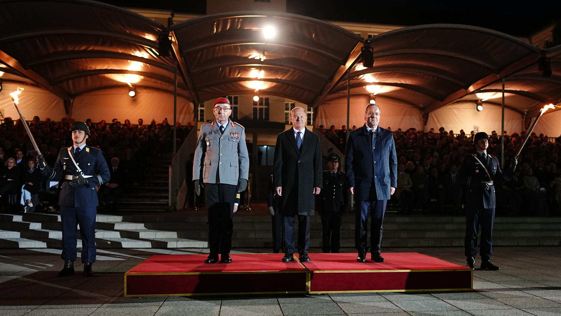 Scholz steht mit Verteidigungsminister Pistorius und General Breuer beim großen Zapfenstreich auf einem Podest.