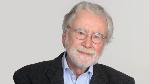 Studioportrait von Dr. Kroener, er trägt einen grauen Anzug, ein hellblaues Hemd und Bart und schaut freundlich in die Kamera