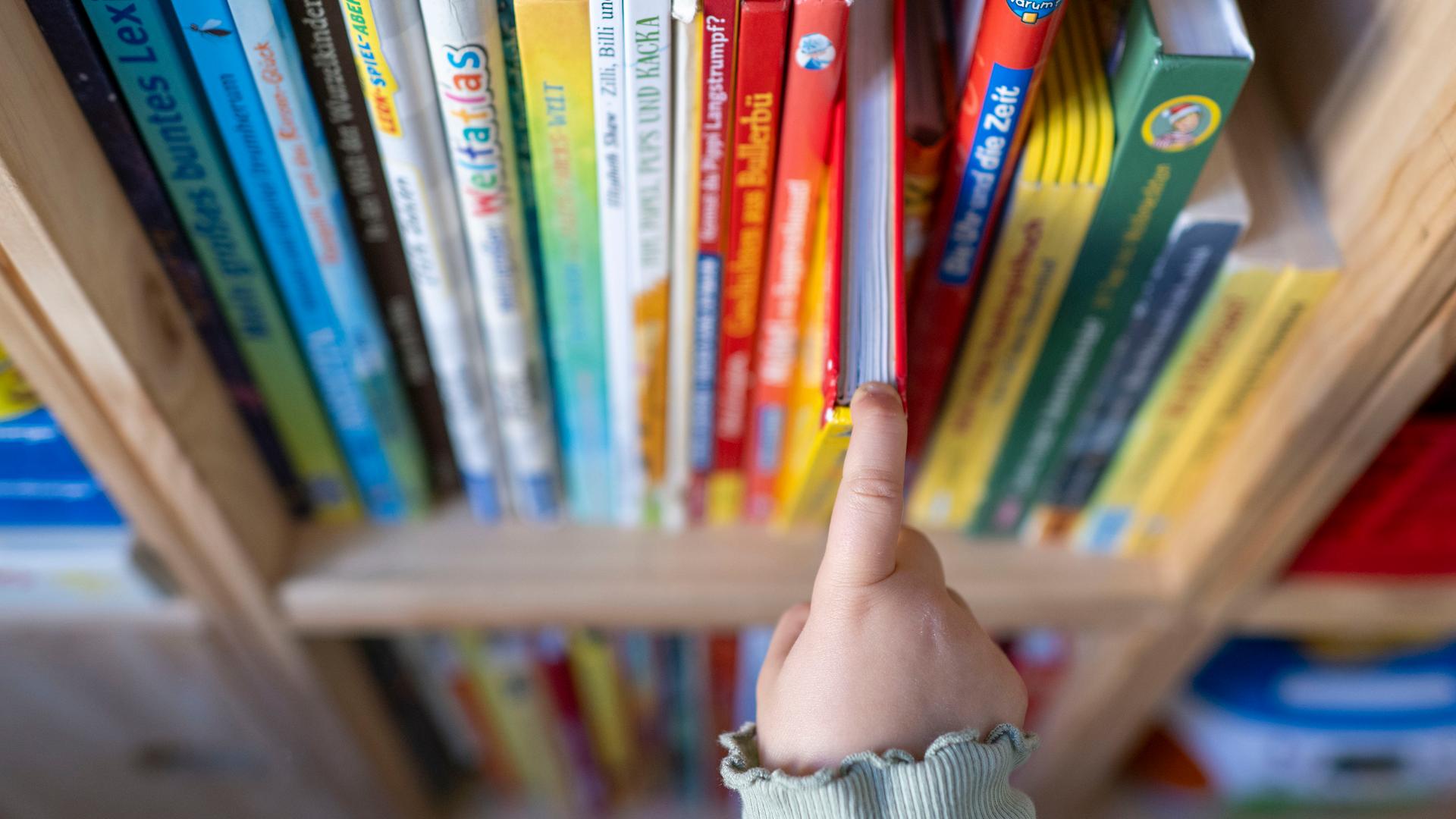 Ein Mädchen zieht in einem Kinderzimmer ein Kinderbuch aus einem Regal.