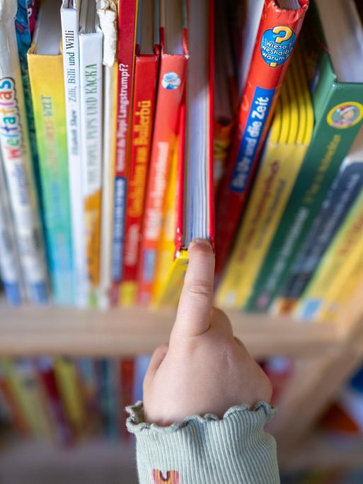 Ein Mädchen zieht in einem Kinderzimmer ein Kinderbuch aus einem Regal.