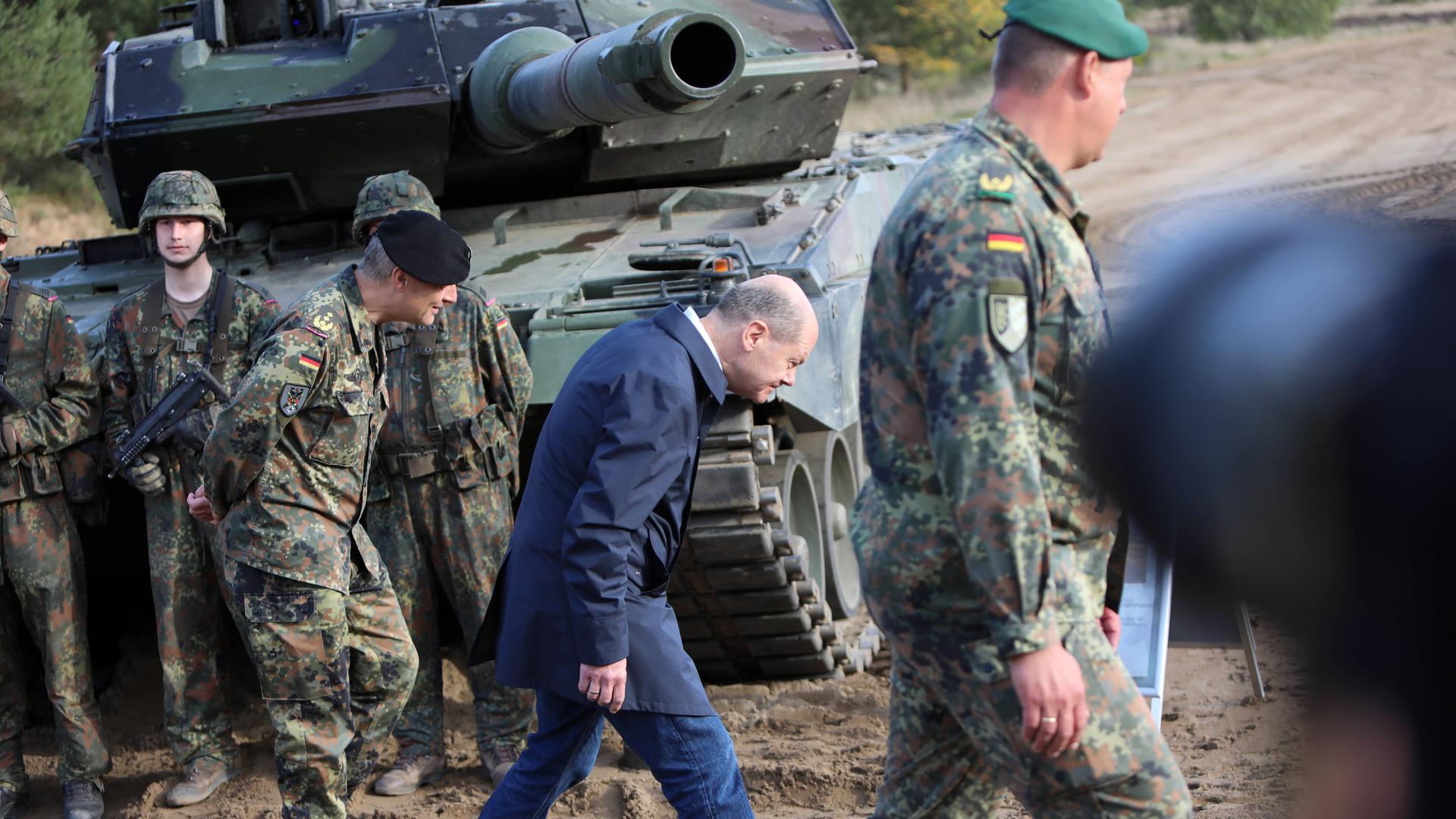 Der deutsche Bundeskanzler Olaf Scholz geht unter der Kanone eine Leopard 2 Kampfpanzers mit eingezogenem Kopf hindurch.