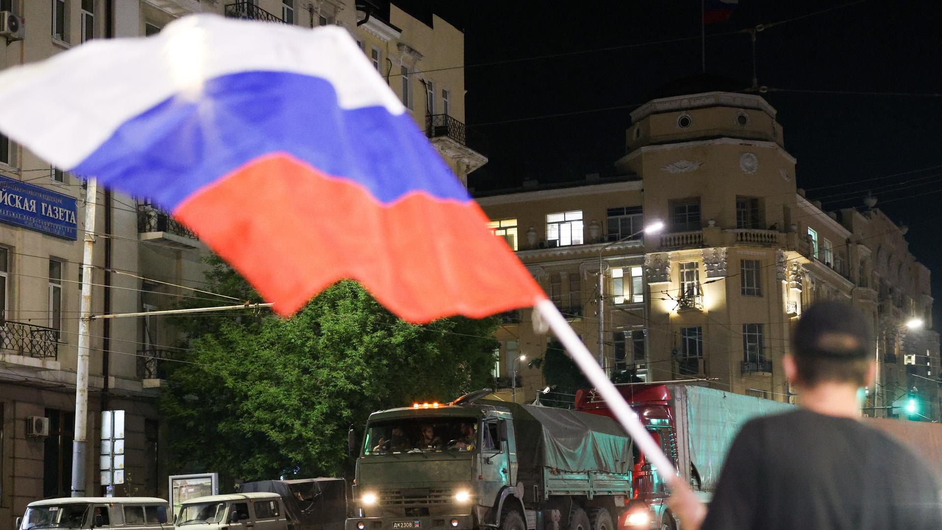 Miltiärfahrzeuge fahren durch die Straßen, ein Mann schwengt die russische Flagge.