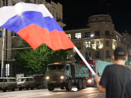 Miltiärfahrzeuge fahren durch die Straßen, ein Mann schwengt die russische Flagge.
