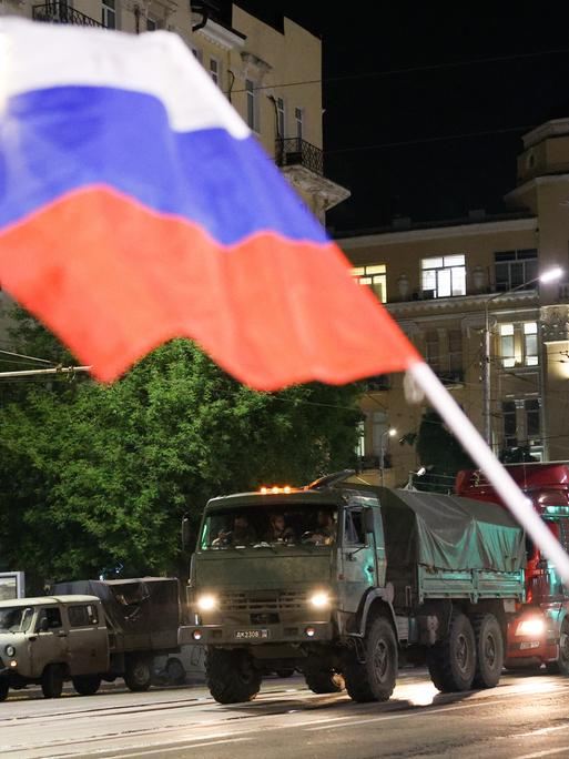 Miltiärfahrzeuge fahren durch die Straßen, ein Mann schwengt die russische Flagge.