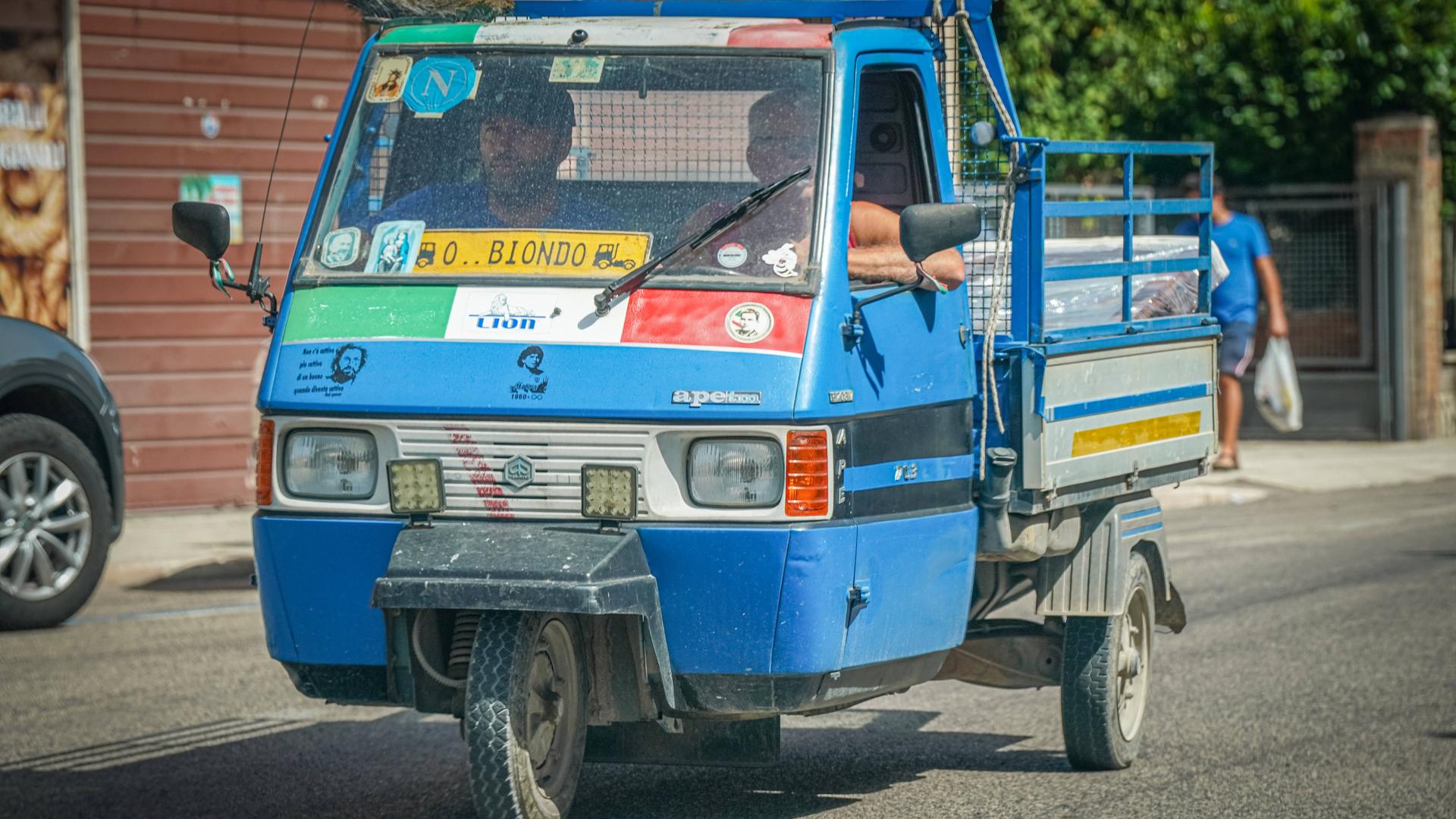 Zwei Männer fahren in Italien in einer blauen "Ape" von Piaggio.