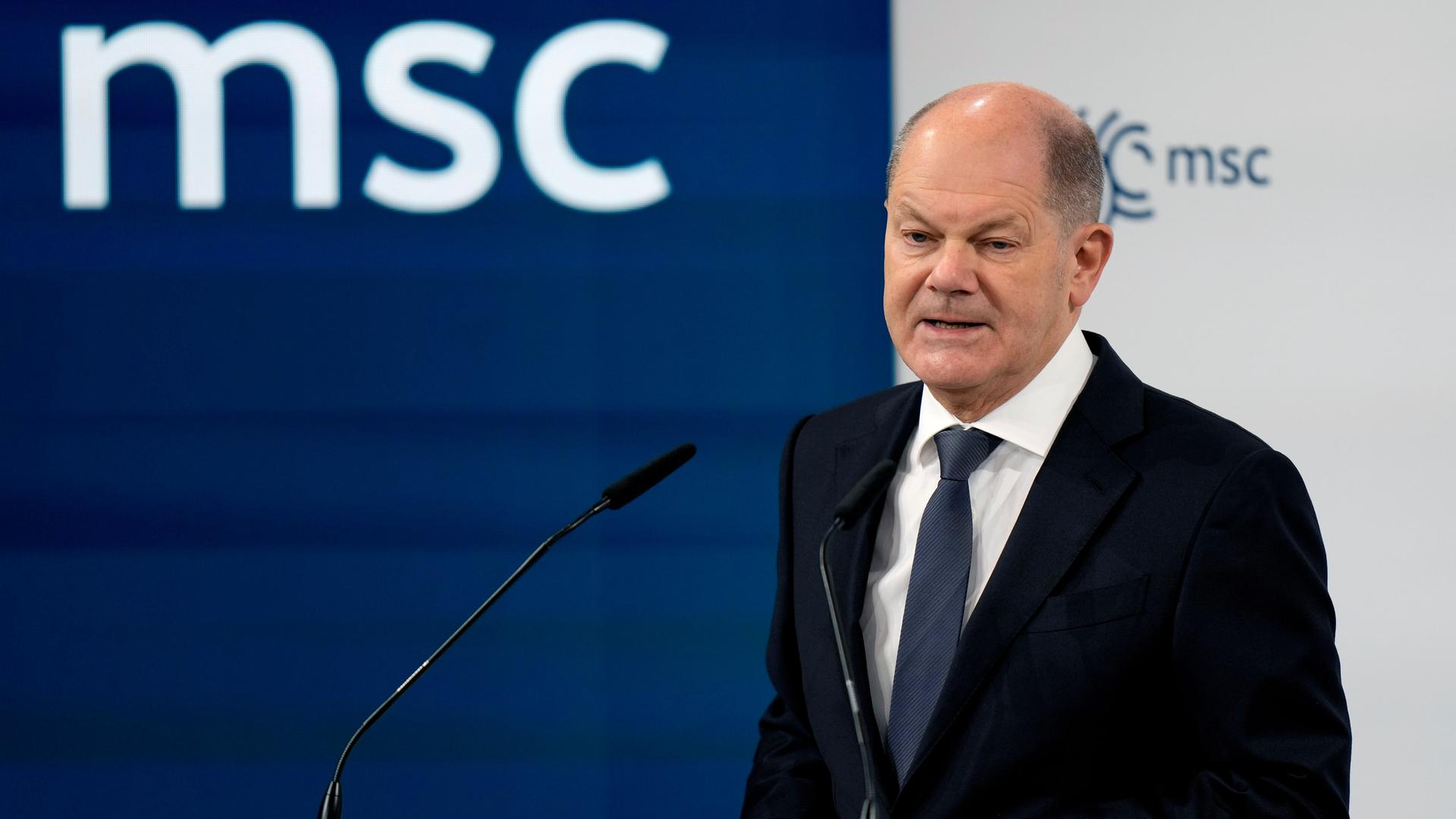 Bundeskanzler Scholz spricht auf der Münchner Sicherheitskonferenz. Im Hintergrund ist das weiße Logo "msc" auf dunkelblauem Grund zu sehen.