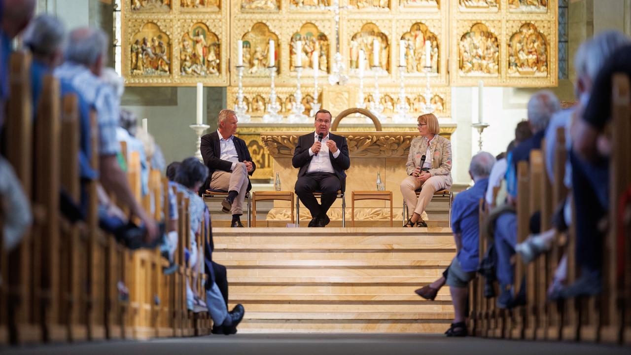 Bei einer Podiumsdiskussion in einem Kirchengebäude sitzen drei Personen auf dem Podium.