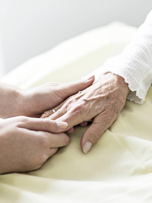 Die Hand einer Pflegerin hält die Hand einer Seniorin.