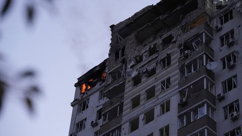 Die Fassade eines Hochhauses in Kiew. Sämtliche Fenster wurden bei den Angriffen zerstört. Der obere Gebäudeteil zeigt massive Zerstörung. In einem Teil des Gebäudes brennt es.