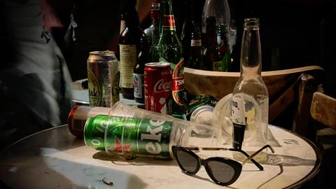 Auf einem runden Tisch stapeln sich Flaschen, Bierdosen und leere Getränkebecher.