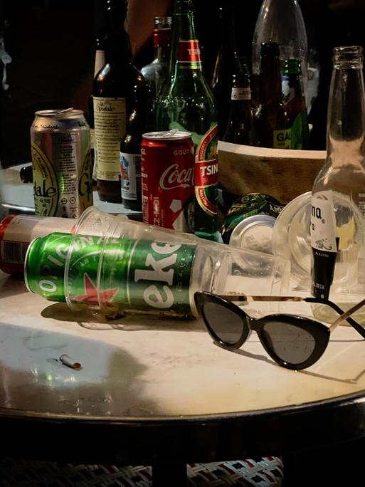 Auf einem runden Tisch stapeln sich Flaschen, Bierdosen und leere Getränkebecher.