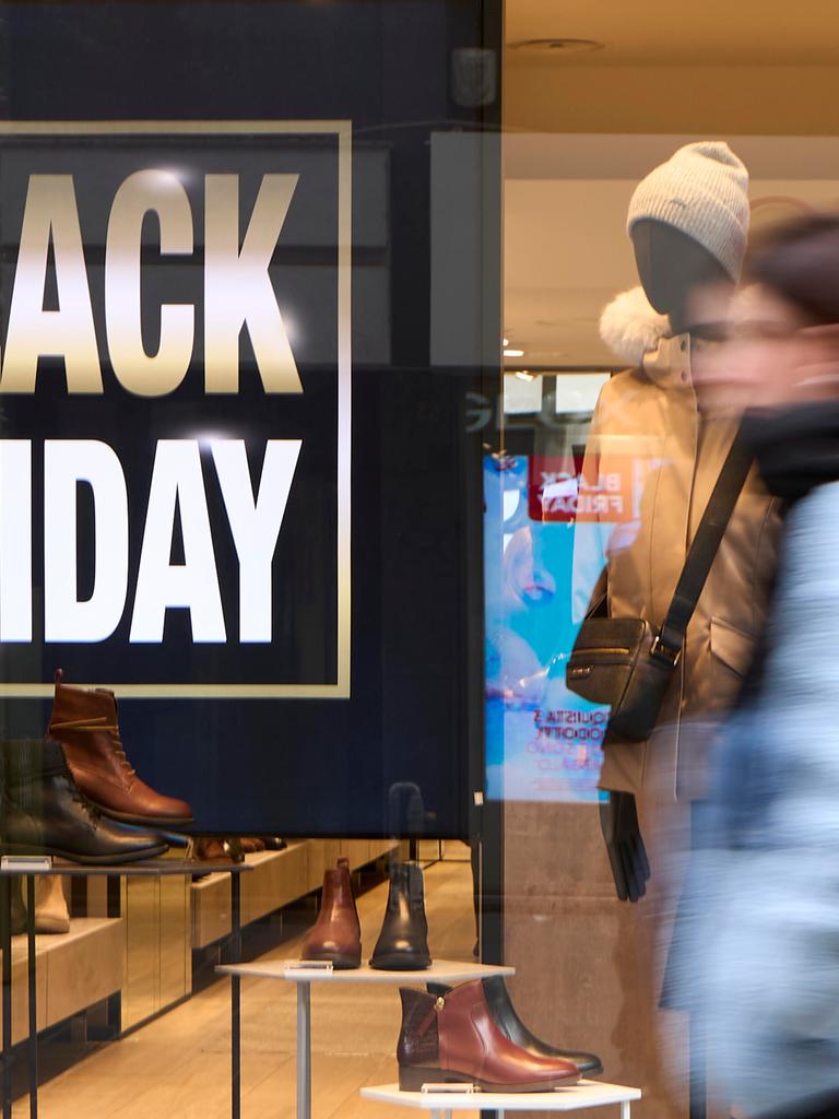 Fußgänger in Winterkleidung laufen an einem hell erleuchteten Schuhladen vorbei; im Schaufenster sind ein großes „BLACK FRIDAY“-Schild und Lederschuhe zu sehen. Fußgänger in Winterkleidung laufen an einem hell erleuchteten Schuhladen vorbei; im Schaufenster sind ein großes „BLACK FRIDAY“-Schild und Lederschuhe zu sehen.