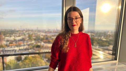 Portrait einer jungen Frau mit rotem Pullover vor einem Fenster im Sonnenlicht