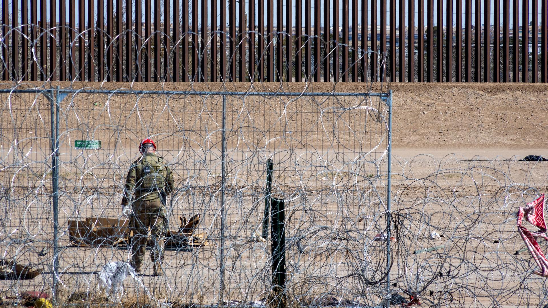 Ein Mitglied der texanischen Nationalgarde patrouilliert zwischen einem stacheldrahtbewehrten Zaun und einer mauerähnlichen Vorrichtung aus Metallstäben.