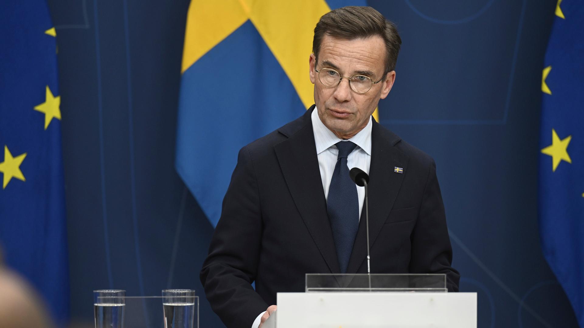 Der schwedische Ministerpräsident Kristersson steht hinter einem Rednerpult. Die schwedische und zwei EU-Fahnen hängen hinter ihm. Der schwedische Ministerpräsident Kristersson steht hinter einem Rednerpult. Die schwedische und zwei EU-Fahnen hängen hinter ihm.