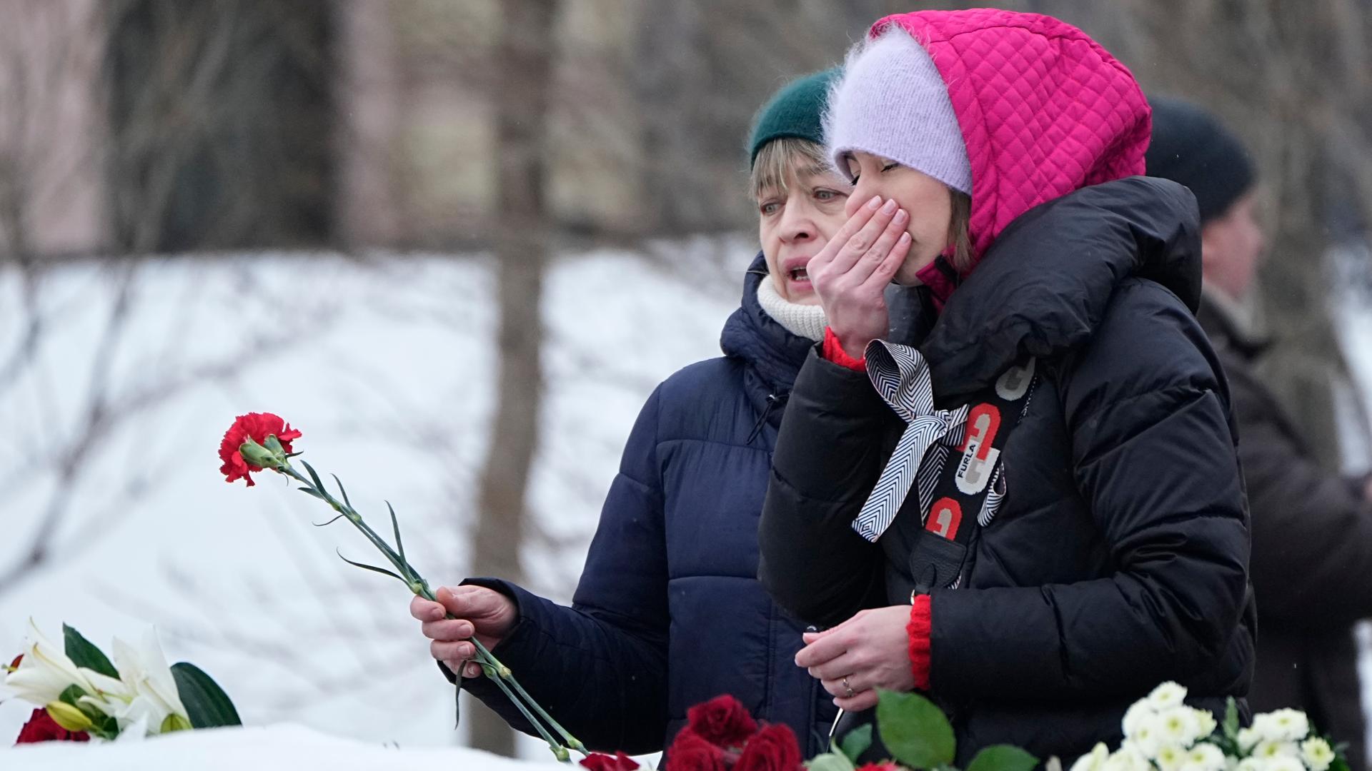 Zwei Frauen legen Blumen an einer Gedenkstätte ab. Sie trauern.