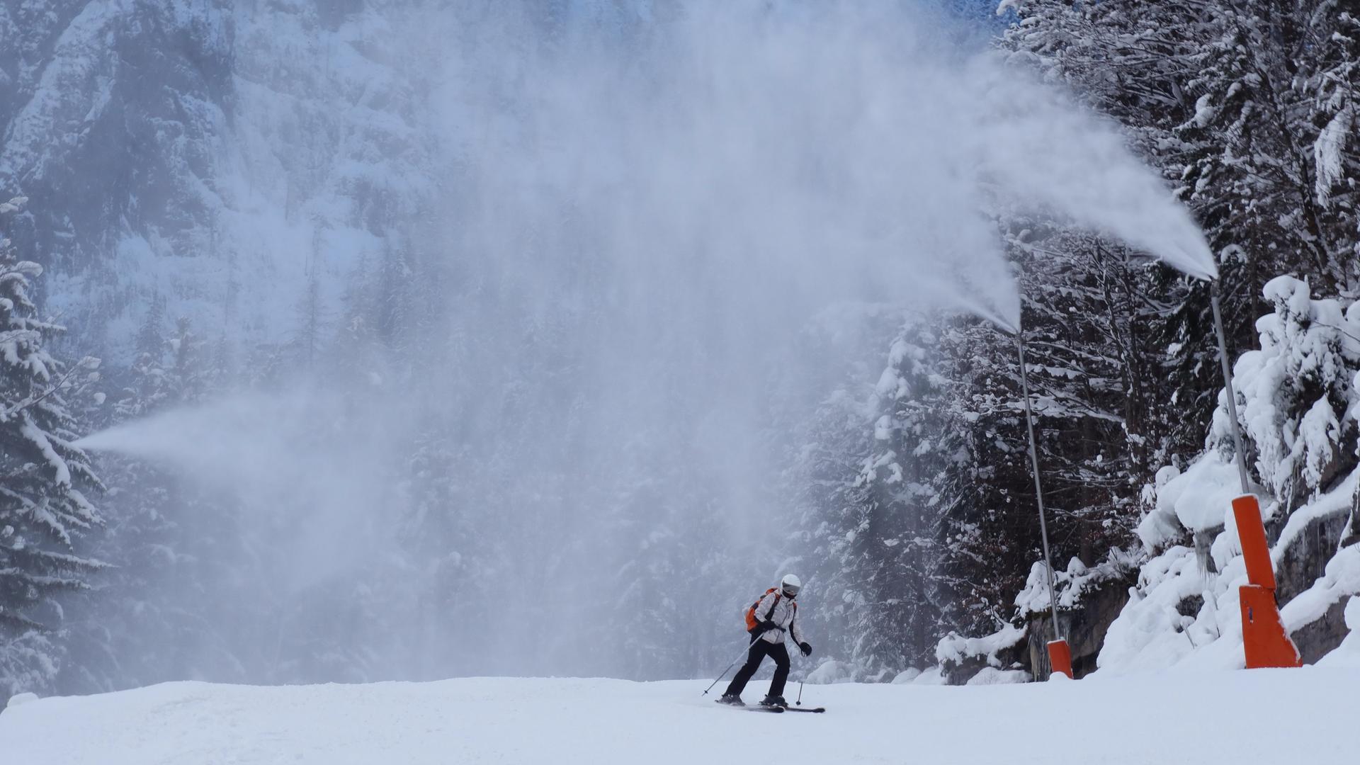 Eine Piste im oberösterreichischen Krippenbrunn wird mit Kunstschnee beschneit; ein Skifahrer gleitet darüber.