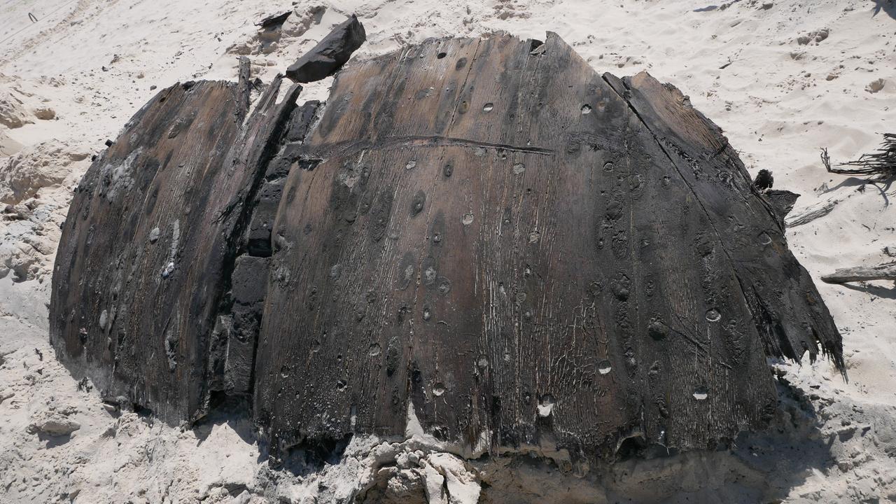 Ein Teil eines rund 300 Jahre alten Schiffswracks liegt am Strand der Nordseeinsel Norderney. Das dunkle Holz ist gebogen. Es liegt im Sand. 
