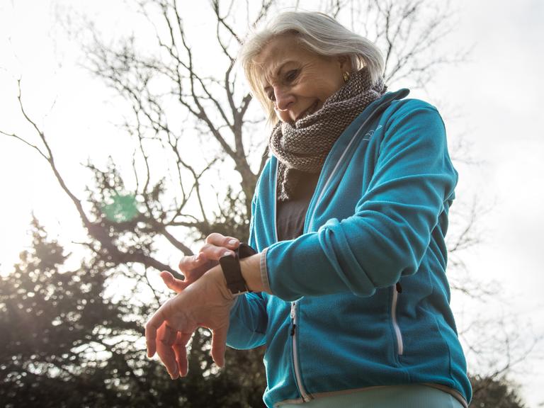 Eine ältere Joggerin in einem Park in Hamburg schaut auf ihr Wearable. (Symbolbild)