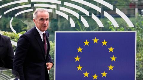 Kanadas Premierminister Mark Carney steht neben einem großen EU-Schild, der Kreis aus gelben Sternen vor blauem Hintergrund.