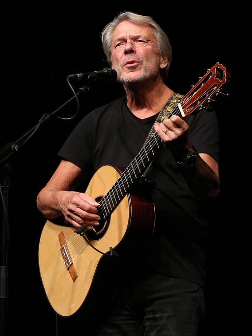 Reinhard Mey singend mit Gitarre auf der Bühne bei einer Tournee 2014.