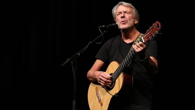 Reinhard Mey singend mit Gitarre auf der Bühne bei einer Tournee 2014.