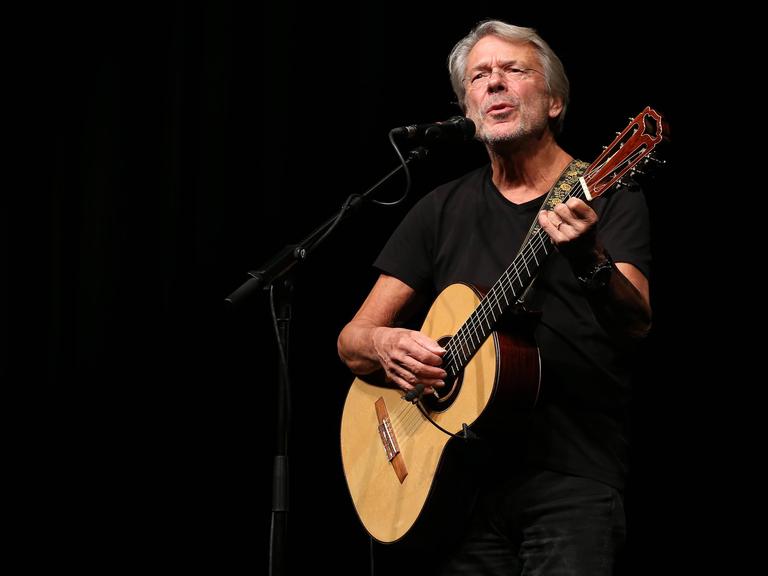 Reinhard Mey singend mit Gitarre auf der Bühne bei einer Tournee 2014.