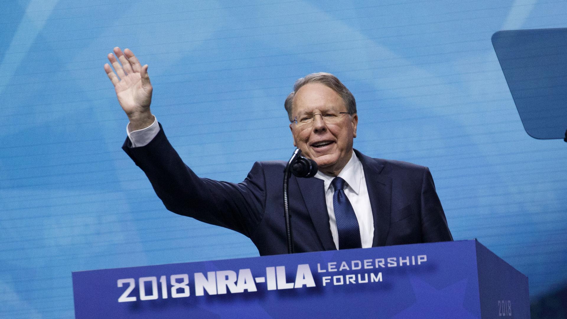 Wayne LaPierre steht hinter einem Rednerpult mit dem Logo der NRA, er winkt mit erhobener rechter Hand in die Menge. Aufnahme vm 04.05.2018 aus Dallas, Texas.