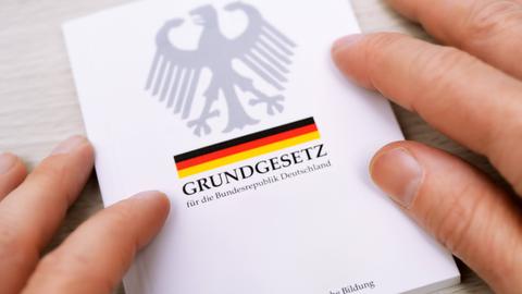 Zwei Hände streichen über die Ränder eines deutschen Grundgesetzes.