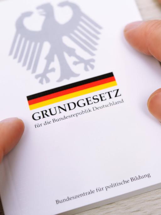Zwei Hände streichen über die Ränder eines deutschen Grundgesetzes.