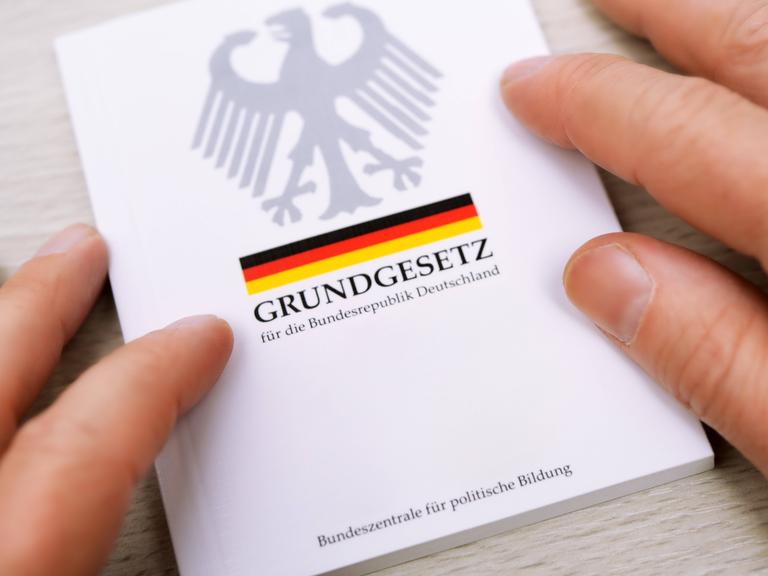 Zwei Hände streichen über die Ränder eines deutschen Grundgesetzes.