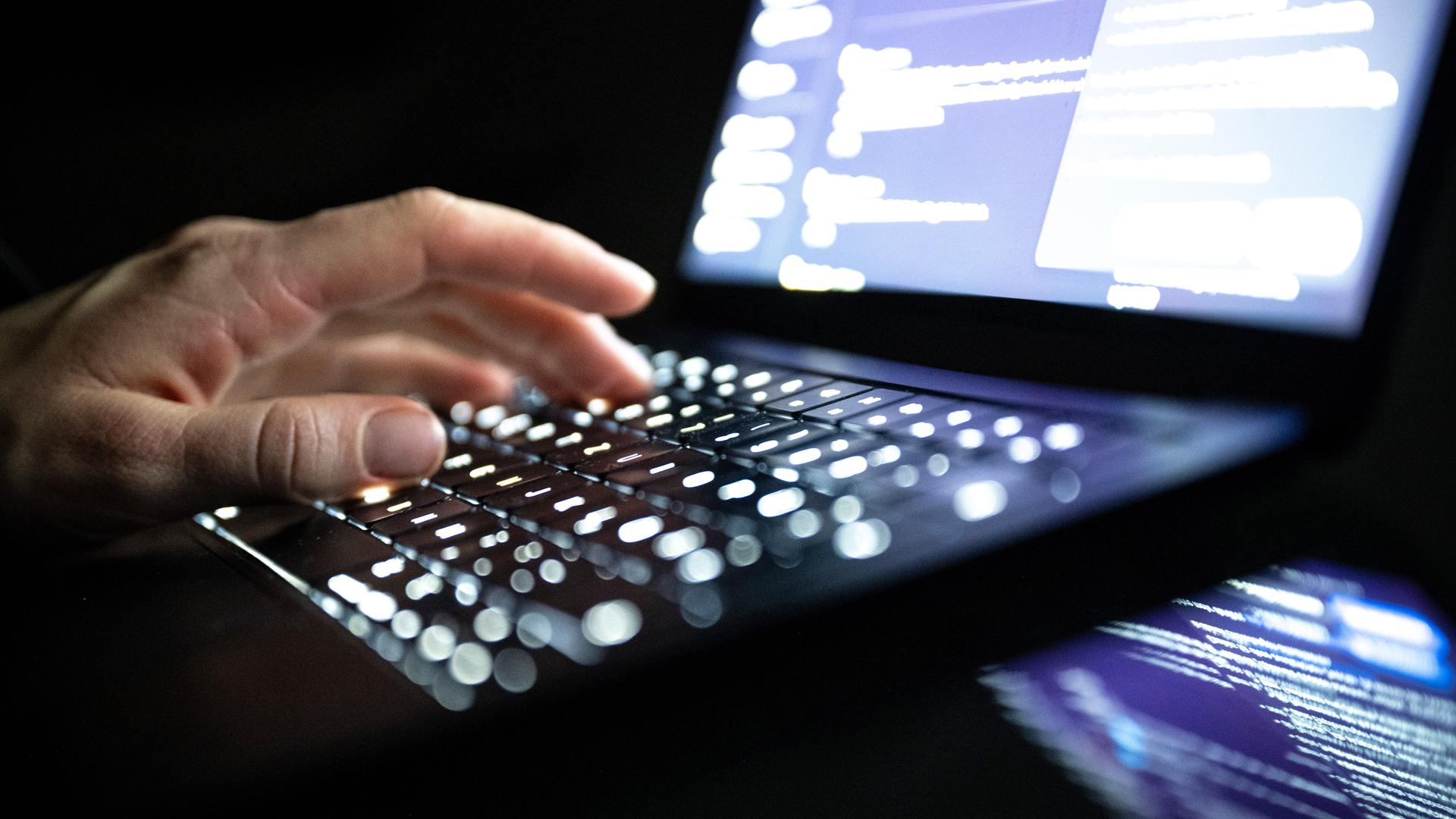 Eine Person tippt mit den Fingern auf einer beleuchteten Laptop-Tastatur. 