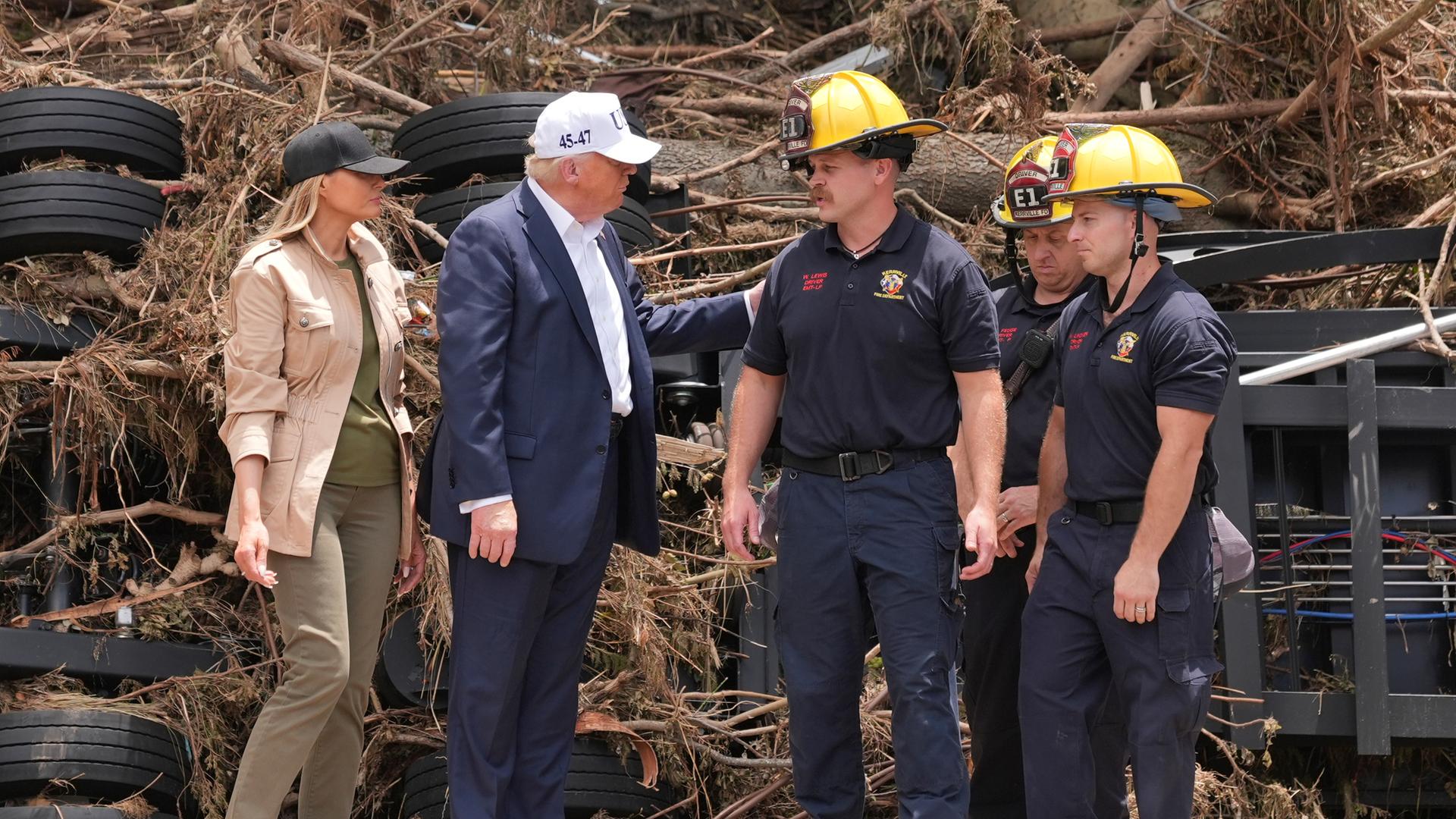 Trump und seine Frau unterhalten sich mit Rettungskräften. Sie stehen nebeneinander.