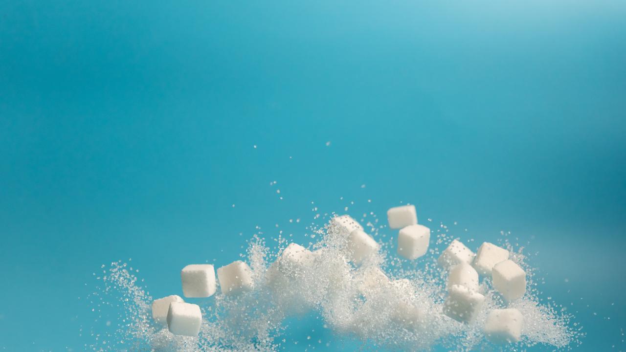 Fliegende und teilweise sich auflösende Zuckerstückchen vor blauem Hintergrund.