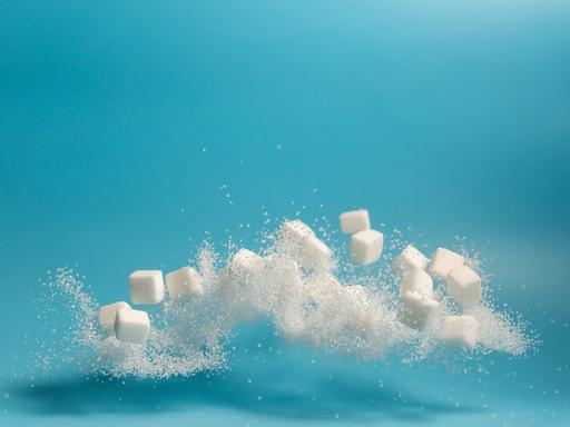 Fliegende und teilweise sich auflösende Zuckerstückchen vor blauem Hintergrund.